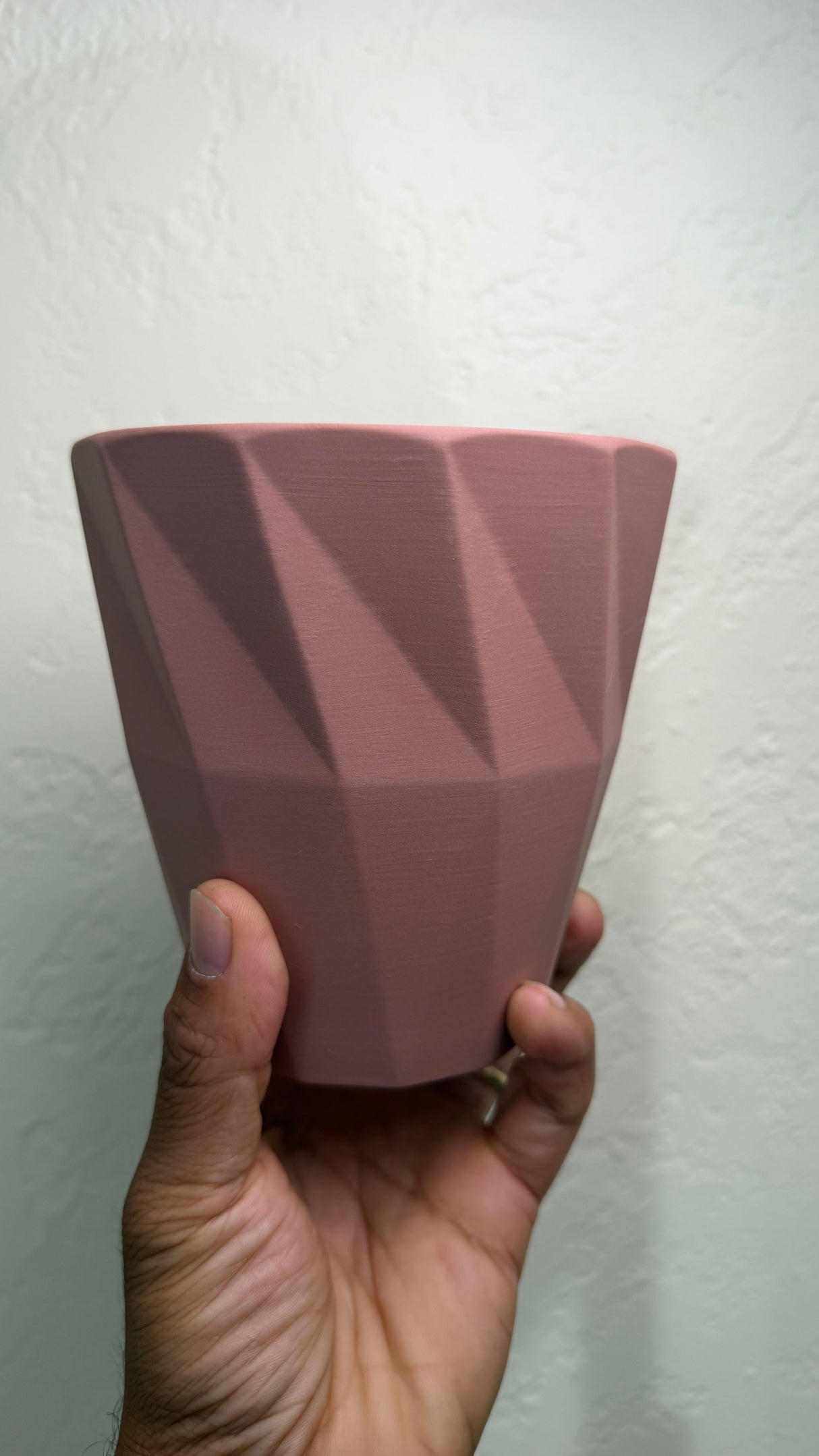 Side view of the pink ceramic pot held in a hand showing the angled geometric facets
