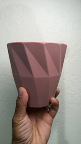 Side view of the pink ceramic pot held in a hand showing the angled geometric facets